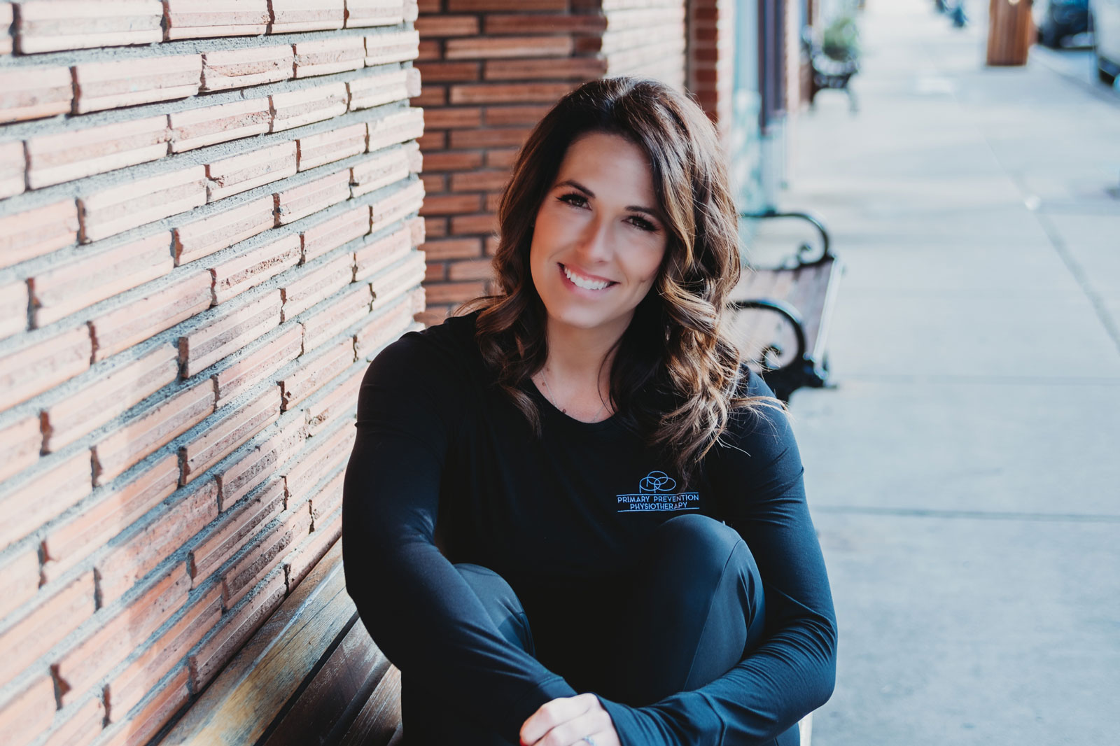 Amber Schlemmer, UM-Flint Alum, smiling while seated outdoors against a brick wall.
