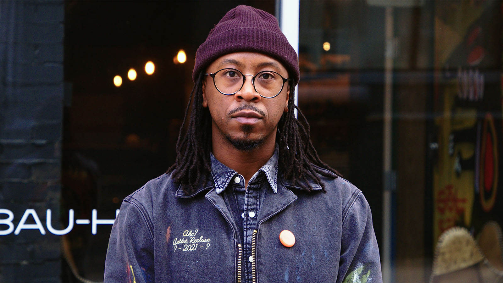 UM-Flint Alumni Lee Grant Allen, standing outdoors in front of a storefront, wearing glasses and a knit cap.